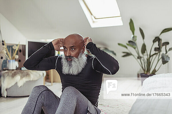 Älterer Mann mit Bart macht Sit-ups auf dem Schlafzimmerboden