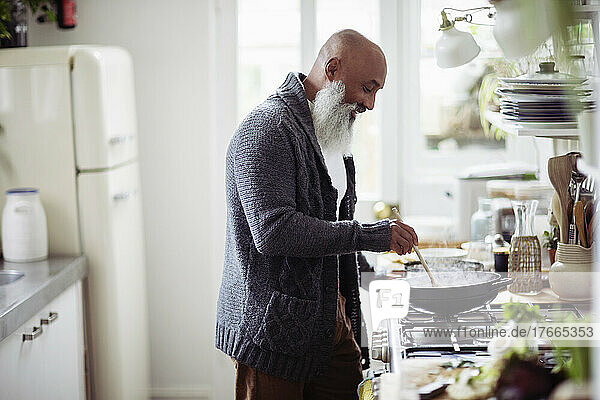 Älterer Mann mit Bart kocht am Küchenherd