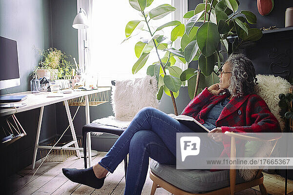 Ältere Frau  die im Sessel im Büro zu Hause ein Buch liest