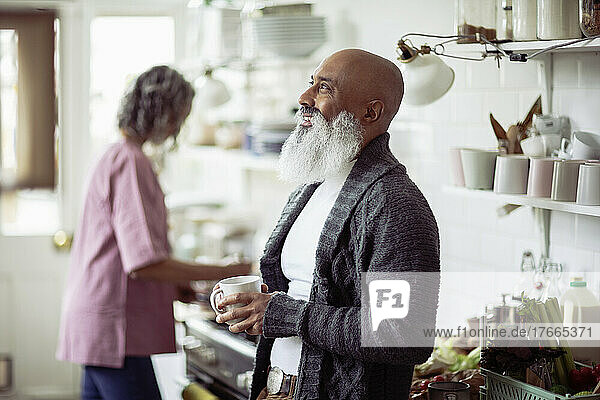 Glücklicher reifer Mann mit Bart trinkt Tee in der Küche