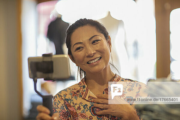Lächelnde Ladenbesitzerin beim Vloggen mit Smartphone und Selfie-Stick