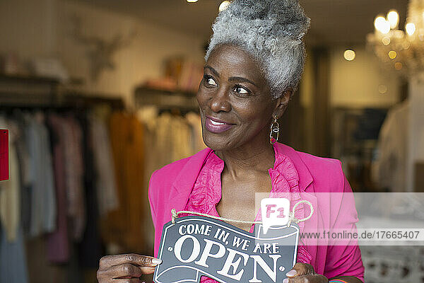 Porträt einer selbstbewussten Geschäftsinhaberin mit offenem Schild in einer Boutique
