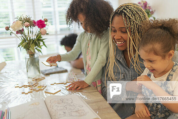 Happy mother and daughters coloring and playing at table