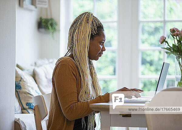 Frau mit blonden Zöpfen arbeitet von zu Hause aus am Laptop