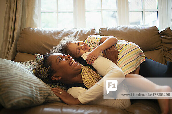 Happy playful mother and daughter on living room sofa