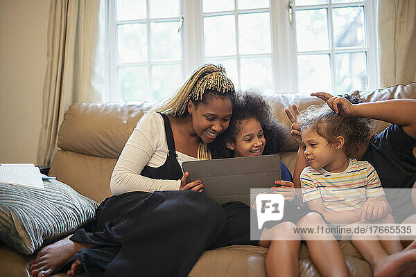 Mutter und Töchter benutzen ein digitales Tablet auf dem Wohnzimmersofa