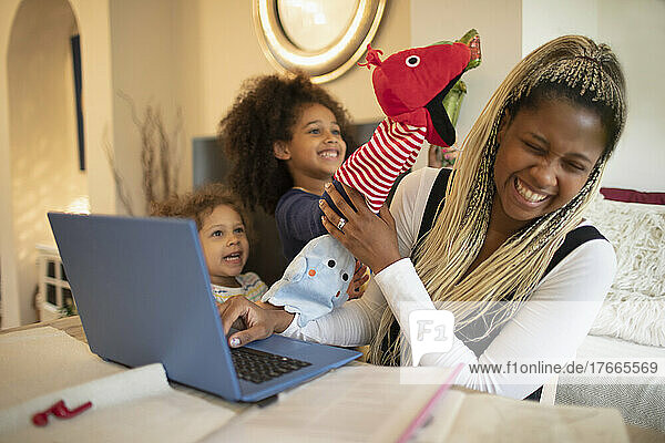 Playful daughters with puppets distracting mother working at laptop