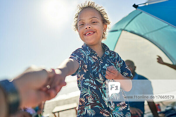 POV portrait cute  happy boy with Down Syndrome holding hands on beach