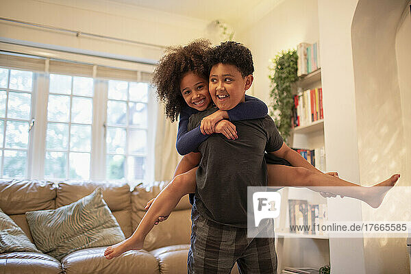 Portrait happy brother piggybacking sister in living room