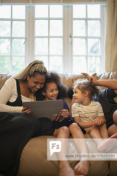 Mother and daughters using digital tablet on living room sofa