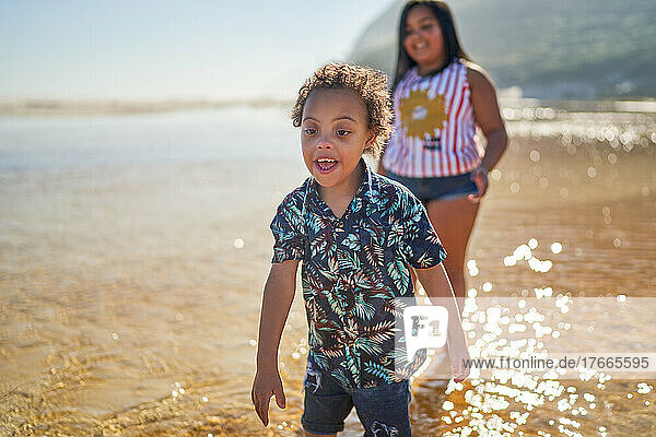 Happy brother with Down Syndrome and sister playing in sunny ocean