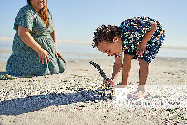 Boy with Down Syndrome drawing in sand with stick on sunny beach