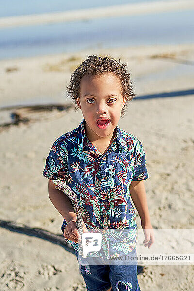 Portrait cute boy with Down Syndrome holding stick on beach