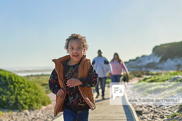Portrait carefree boy with Down Syndrome running on beach boardwalk