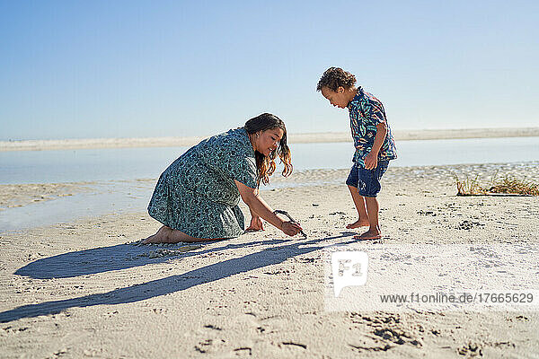 Mother and son with Down Syndrome drawing in sand with stick on beach
