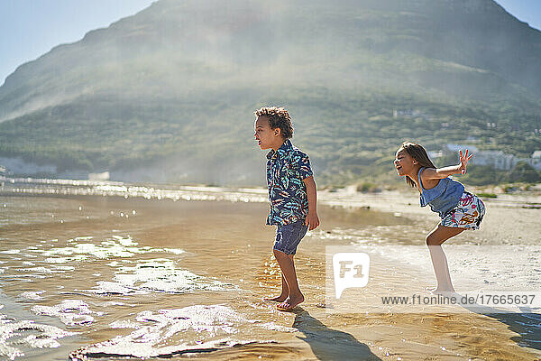 Brother and sister playing in sunny ocean surf on beach