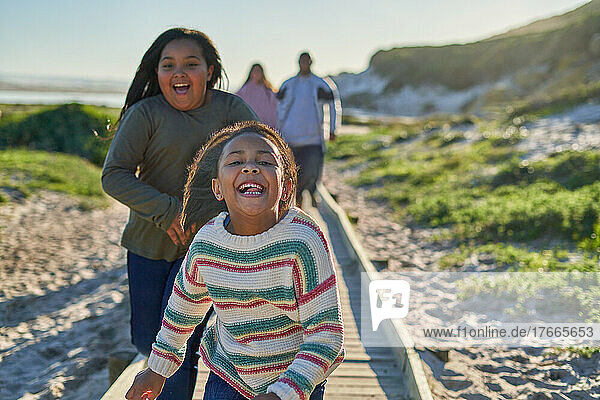 Portrait carefree sisters running on sunny beach boardwalk