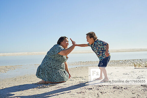 Happy mother and son high fiving on sunny ocean beach