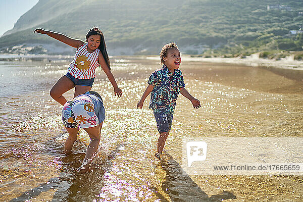 Happy sisters and brother with Down Syndrome playing in ocean surf