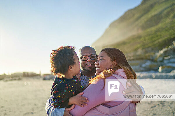 Happy parents and son hugging on sunny beach