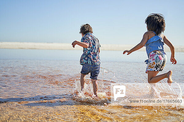 Brother and sister running in sunny ocean surf