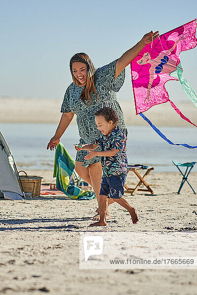 Happy mother and son playing with kite on sunny beach
