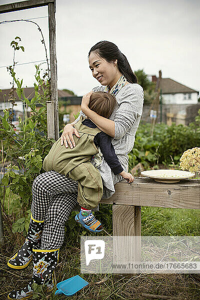 Happy mother holding tired toddler son on bench in garden
