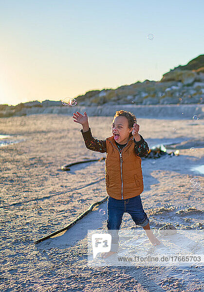Happy  carefree boy with Down Syndrome playing with bubbles on beach
