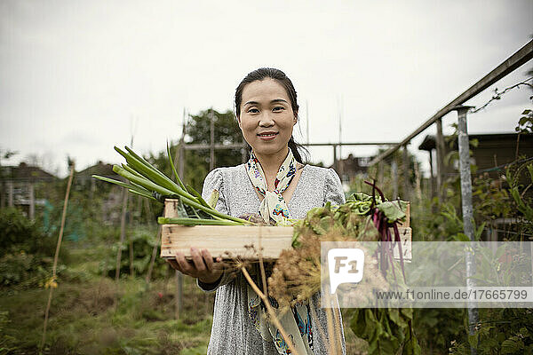 Portrait smiling woman with harvested vegetables in garden