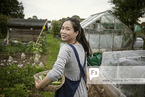 Portrait happy woman with basket of harvested vegetables in garden