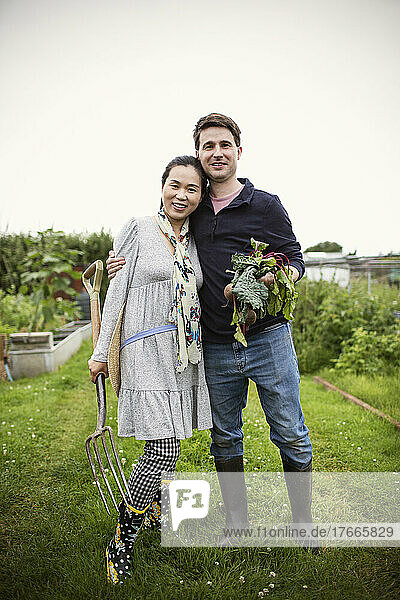 Portrait happy couple with harvested vegetables in garden