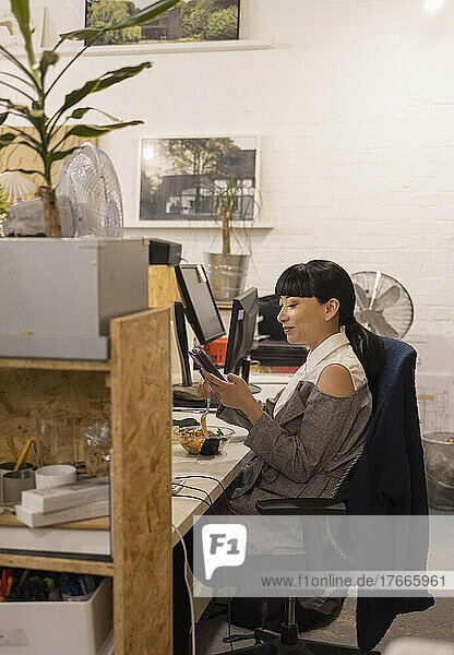 Businesswoman using smart phone at office desk