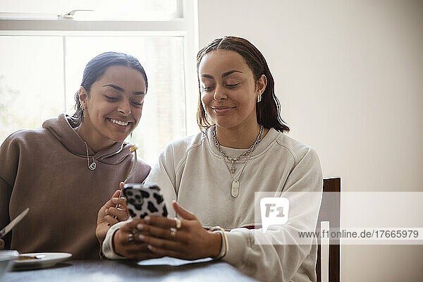 Smiling young adult sisters using smart phone at home