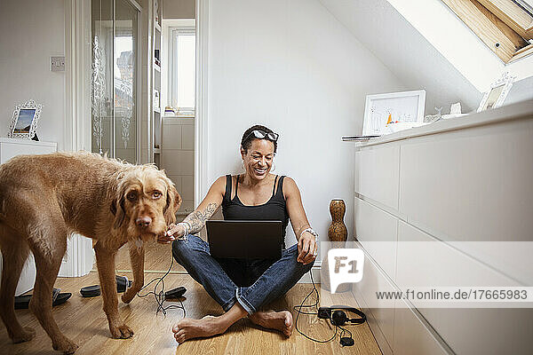Happy woman with dog and laptop on bedroom floor