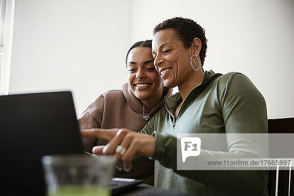 Happy mother and young adult daughter using laptop