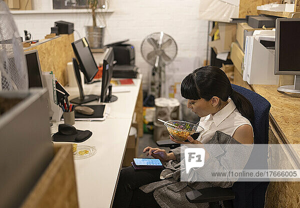 Businesswoman eating lunch and using smart phone in office