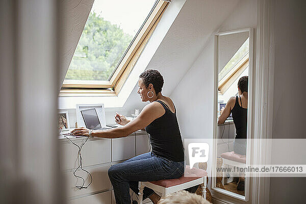 Mature woman working from home at laptop below skylight