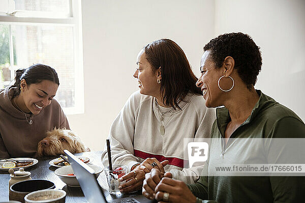 Mother and young adult daughters with dog at dining table