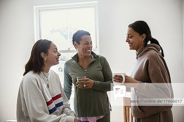 Happy mother and young adult daughters drinking tea and talking