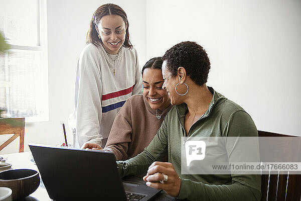 Happy mother and young adult daughters using laptop at home