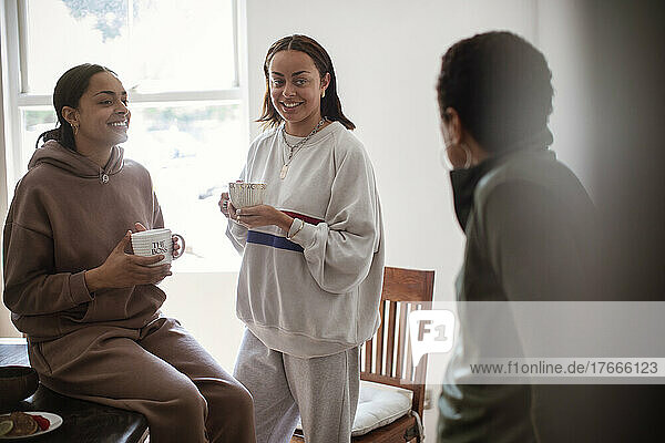 Smiling mother and daughters talking and drinking coffee at home