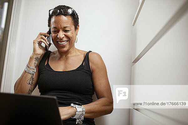 Smiling woman talking on smart phone at laptop