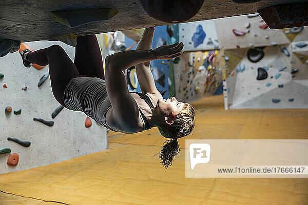Young woman hanging upside-down from rock wall
