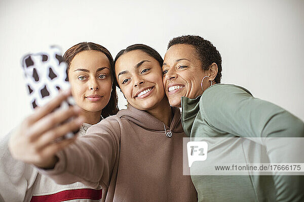 Happy mother and young adult daughters taking selfie with smart phone