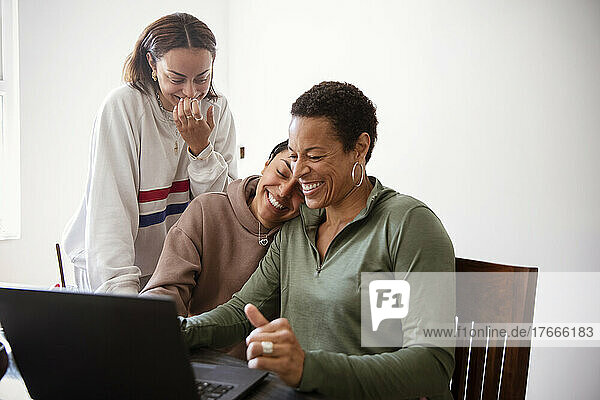 Happy mother and daughters using laptop in dining room