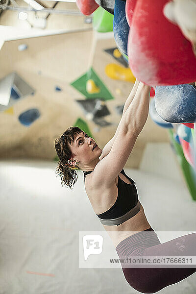 Young female rock climber hanging from climbing wall