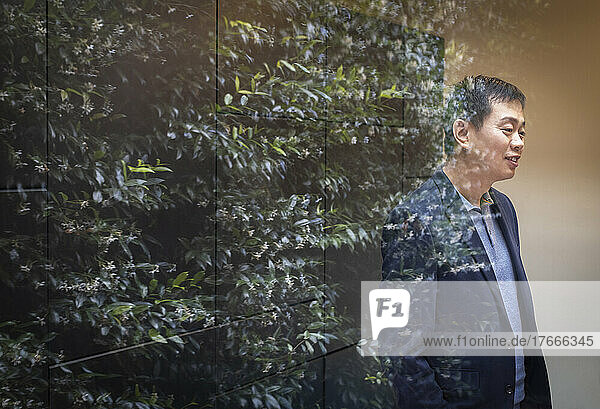 Businessman standing at window with reflection of tree
