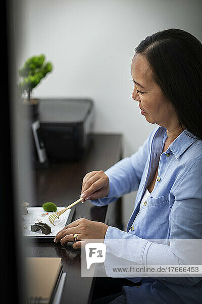 Businesswoman raking zen garden at office desk