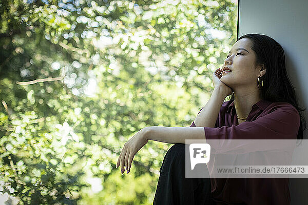 Thoughtful young woman looking at tree from window