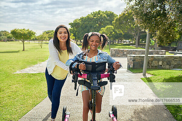 Happy mother and disabled daughter walking with rollator in sunny park